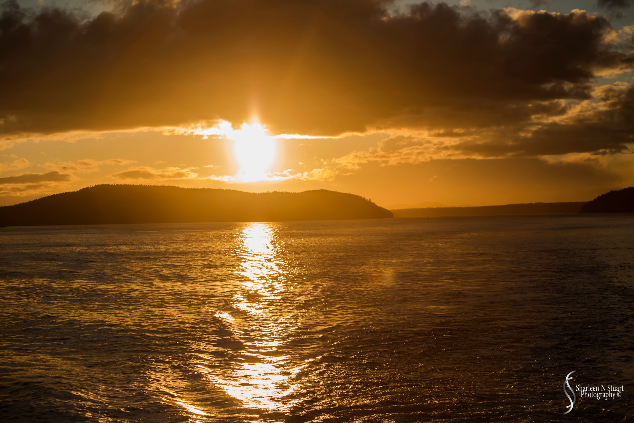 The sun dipped below the clouds and the reflection bathed on the wake of the boat.