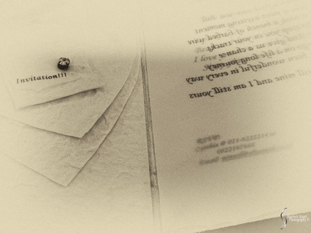 Close-up of an invitation card pinned to textured paper, with blurred text in the background.